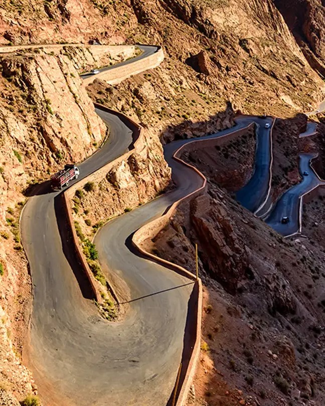 Aerial view of the dramatic, winding road with multiple hairpin turns carved into the steep, red-rock canyon of the Dadès Gorges, Morocco.