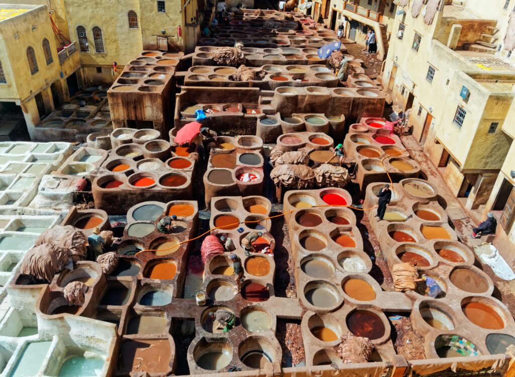 Aerial view of the famous Chouara Tannery in Fes, Morocco, showing the stone vats filled with colorful dyes and workers treating leather.