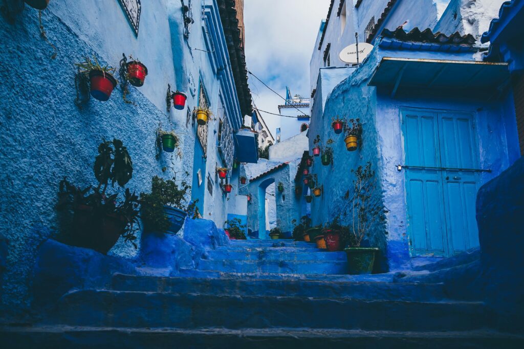 A narrow, blue-washed alley in Chefchaouen, Morocco, showcasing stairs and colorful flower pots, a highlight for cultural tours in Morocco