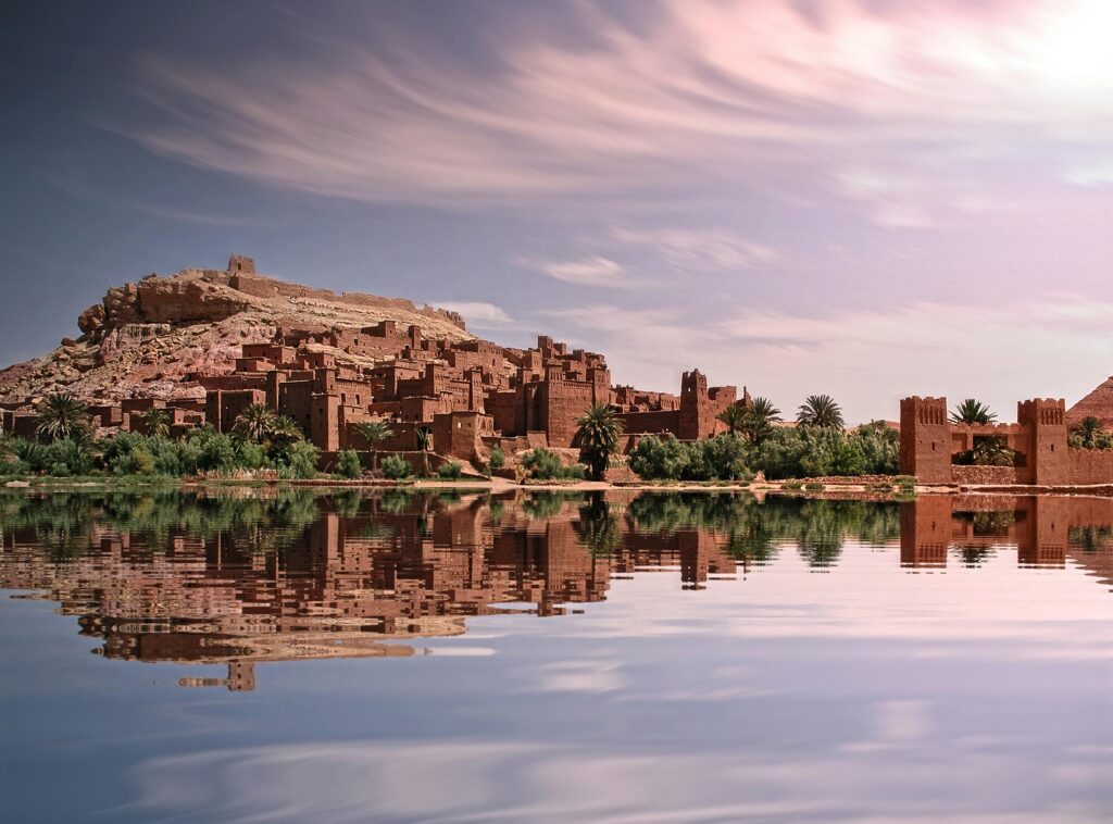 The stunning Ksar of Ait Benhaddou, a UNESCO World Heritage site in Morocco, perfectly reflected in the calm water of a river at sunrise.
